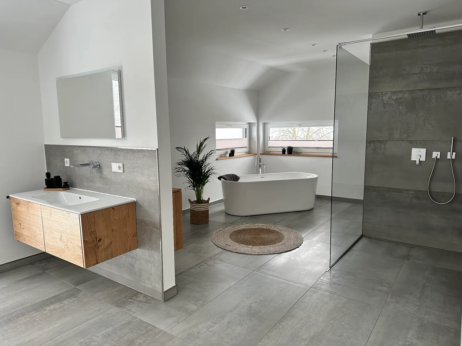 Fertiges Bad mit freistehender Wanne, bodengleicher Dusche hinter Glas und Waschtisch aus Holz
