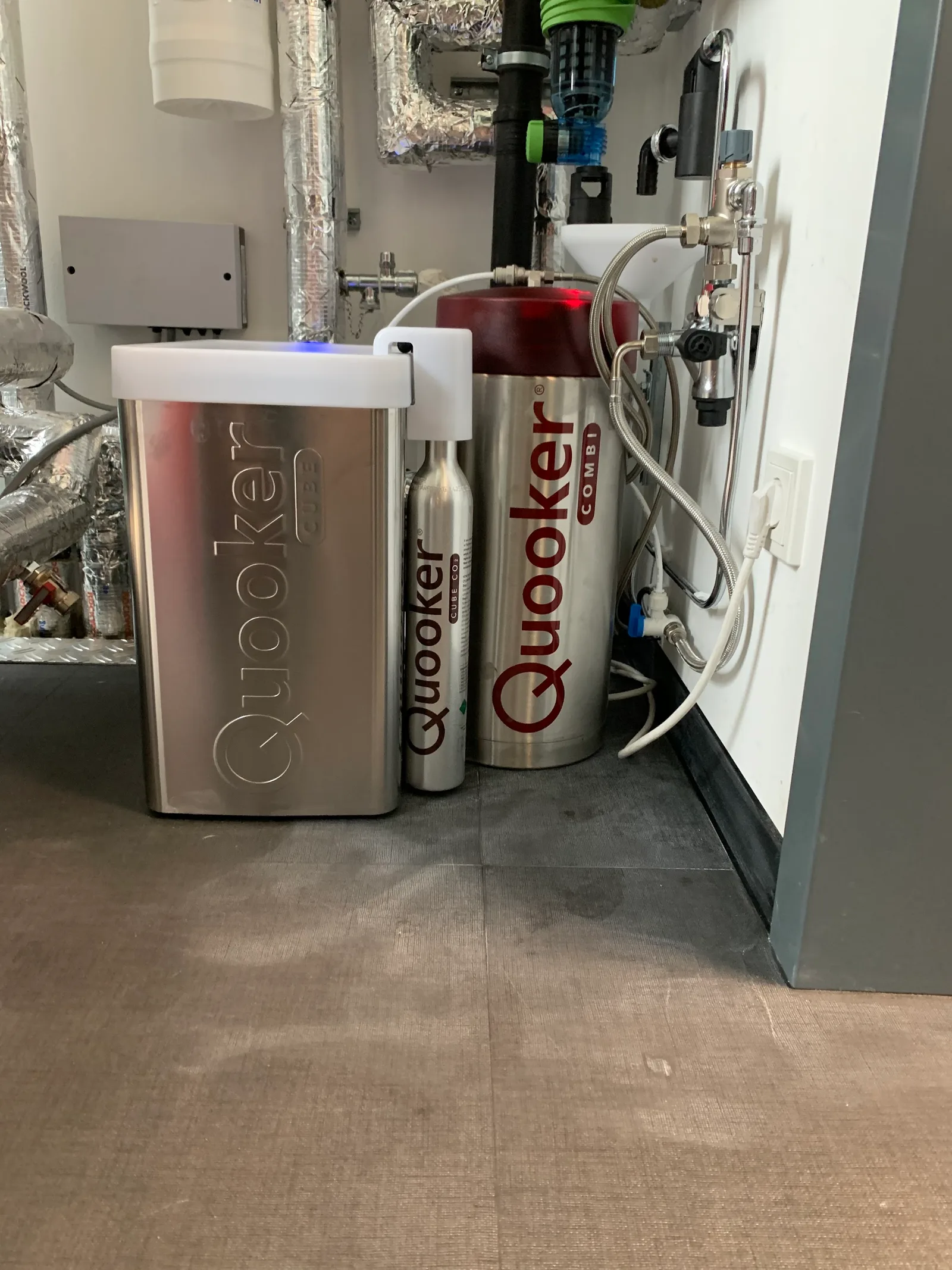 Quooker-Reservoir mit CO₂-Zylinder und Filter an einer Wand mit Wasserleitungen