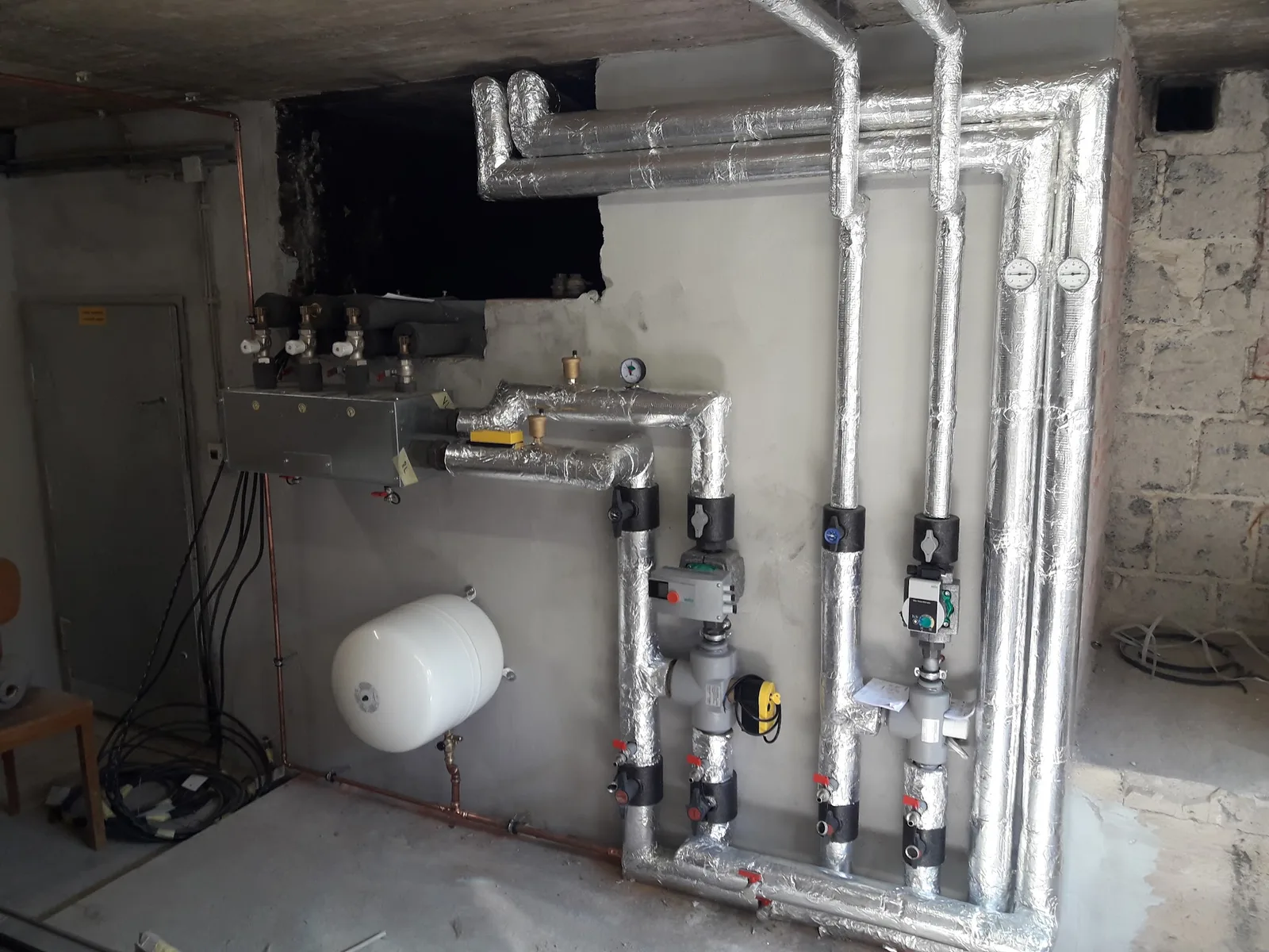 Heizungsverteilung mit gedämmten Rohren, Pumpen und rotem Ausdehnungsgefäß