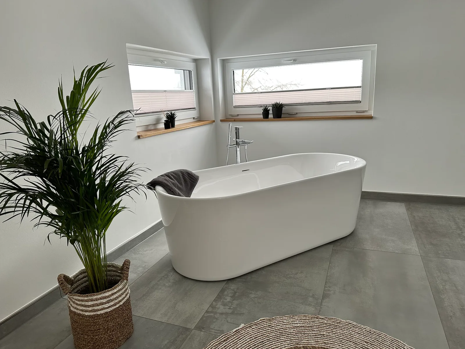 Freistehende weiße Badewanne mit Standarmatur, daneben eine Palme im Korb